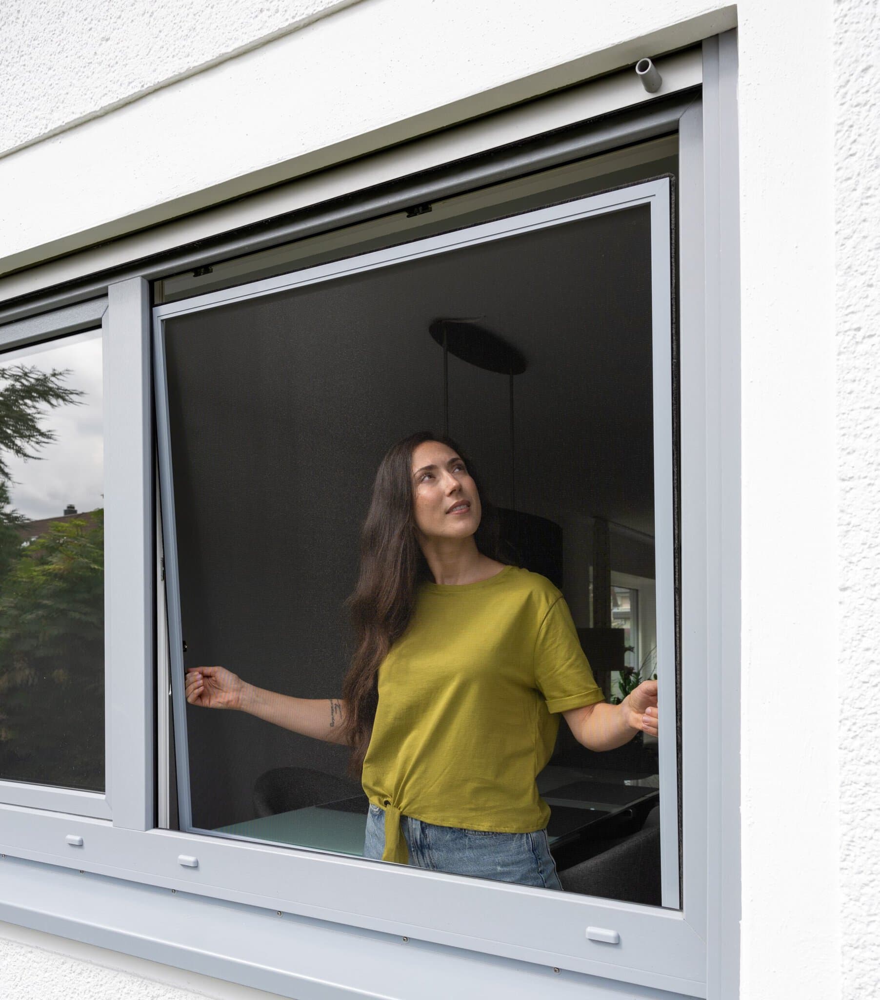 Fliegengitter fürs Fenster, mückenfrei lüften Frau hinter einem Fenster mit Insektenschutzgitter, mückenfrei lüften bei geöffnetem Fenster