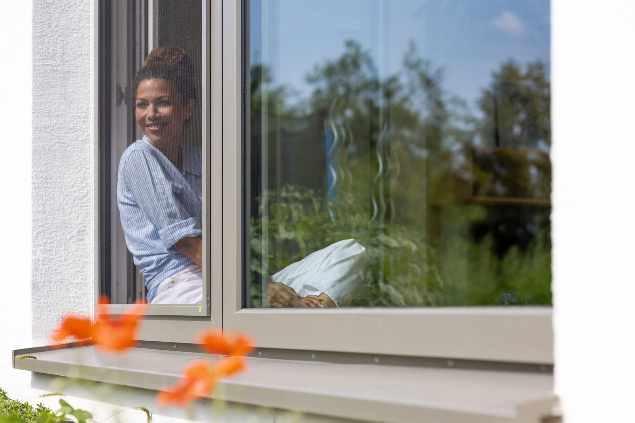 Robuster Aluminiumrahmen in Wunschfarbe Frau am offenen Fenster mit Insektenschutz-Spannrahmen in farbigem Aluminiumrahmen, passend zum Fensterrahmen