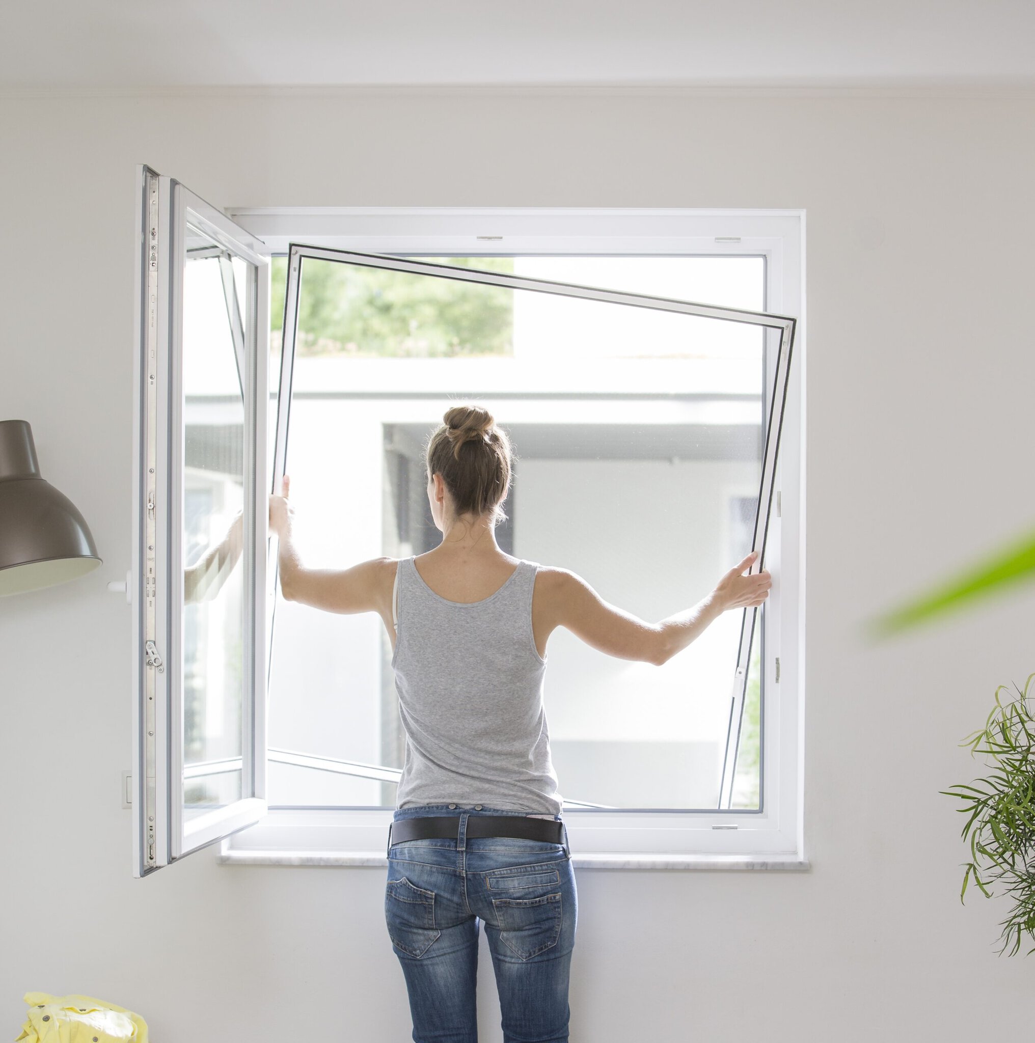 Frau setzt einen Insektenschutz-Spannrahmen von innen ohne Bohren in ihr Fenster ein