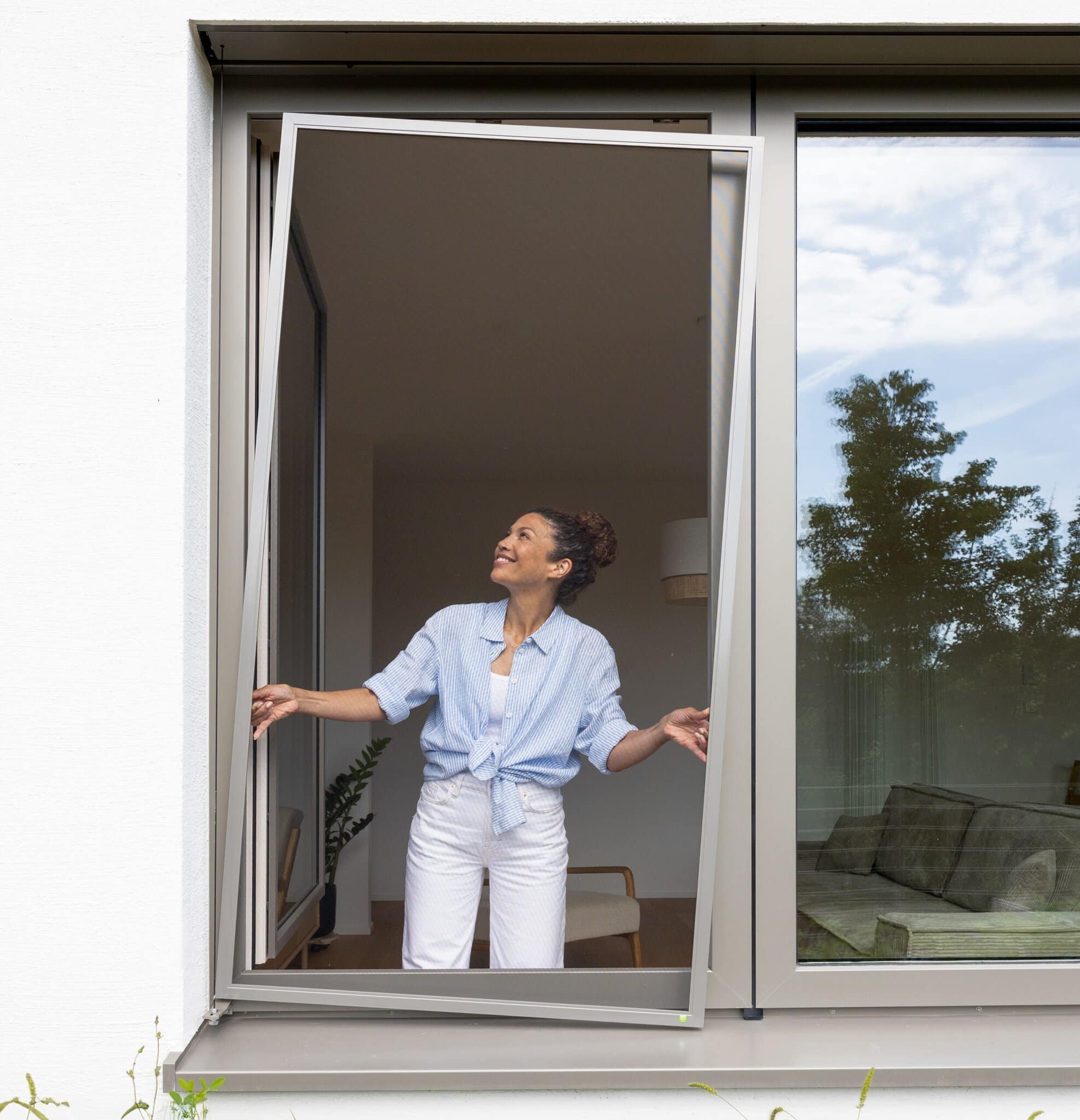 Spannrahmen fürs Fenster, fast unsichtbar Frau am offenen Fenster mit Insektenschutz-Spannrahmen, fast unsichtbares Gewebe mit freiem Blick ins Grüne